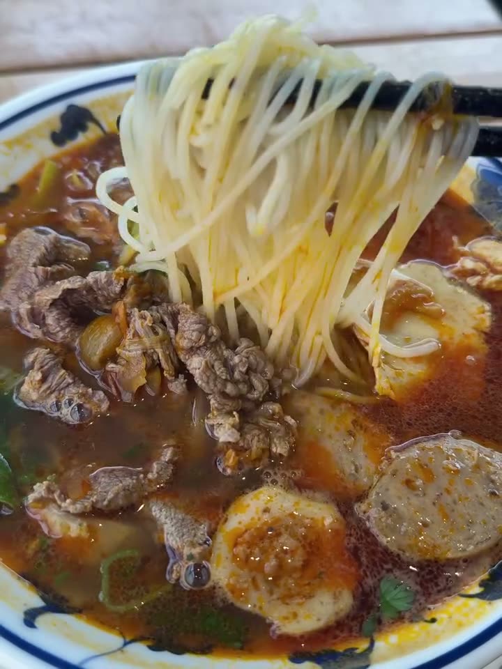 A bowl of bún bò Huế: noodles lifted from a red broth with beef and pork balls